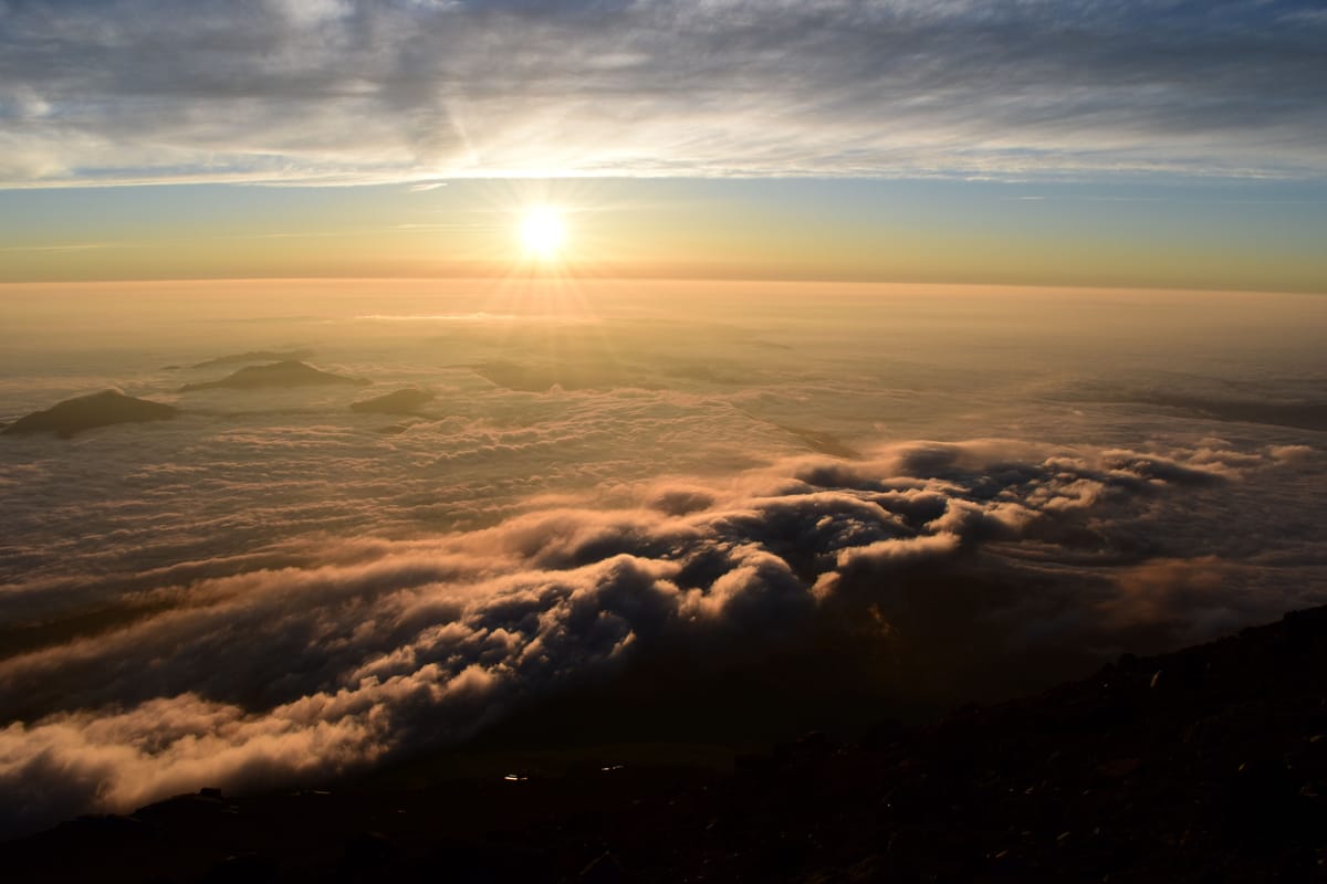 Lever de soleil au-dessus d'une mer de nuages, d'où émergent quelques sommets, vu depuis le haut du mont Fuji