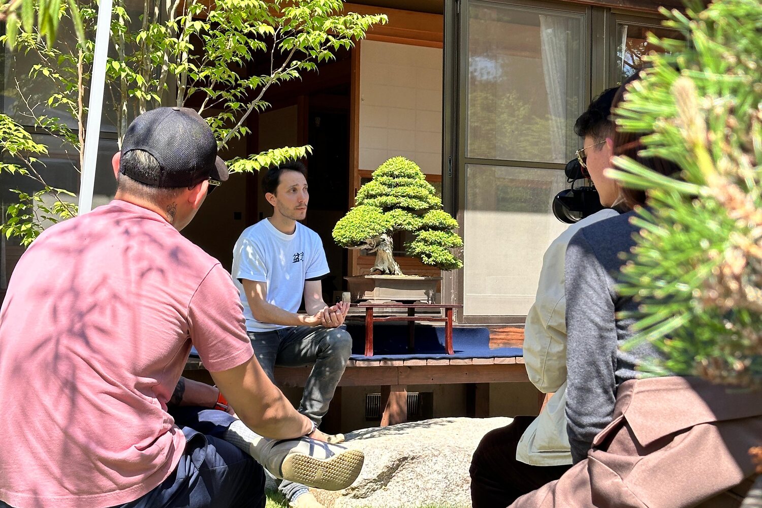 Adrien présente un bonsaï à un petit groupe, dans un jardin au Japon